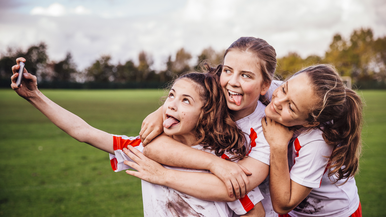 Girls soccer team taking a selfie on smart phone wearing white and red jerseys. 